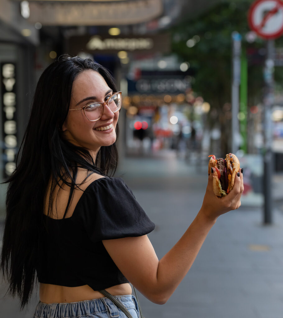 lady holding burger from broadway diner smiling